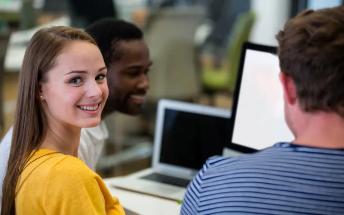3 étudiants autour d'une table : une jeune femme et deux jeunes hommes devant des PC portables
