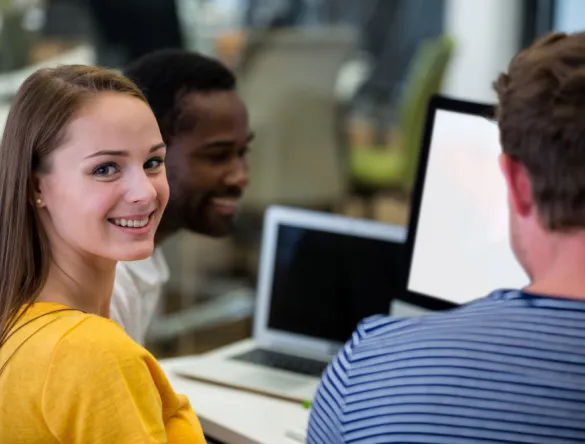 3 étudiants autour d'une table : une jeune femme et deux jeunes hommes devant des PC portables